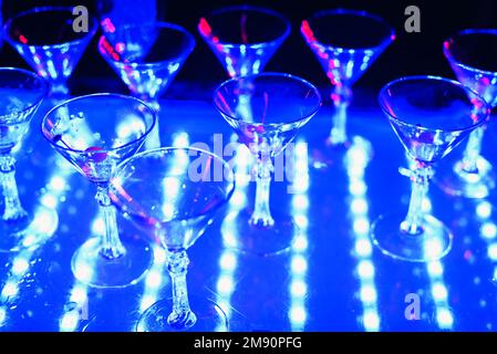 Leere Gläser Cocktails auf der Feiertagsparty mit ultraviolettem Hintergrundlicht Stockfoto