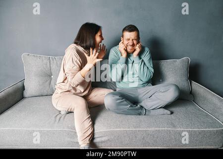 Wütende Frau, die ihren Mann anschreit. Ein Mann, der die Ohren schließt, mit beiden Händen gereizt durch lautes, störendes Geräusch. Beziehungsprobleme, Konflikte, Streit mit CO Stockfoto