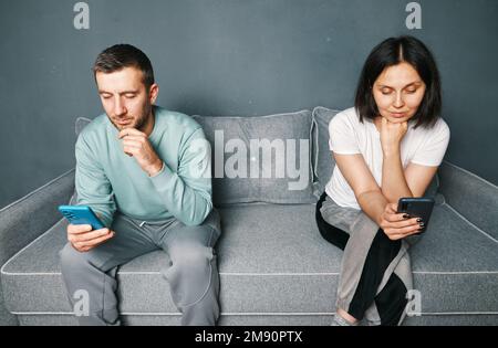 Gelangweiltes junges Paar, das auf der Couch saß und sich zu Hause ihre Smartphones anschaute Stockfoto