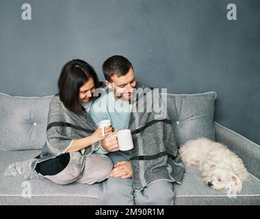 Ein glückliches Familienkonzept. Ein junges Paar, das sich entspannt, Kaffee trinkt und in einem modernen Apartment auf seinen Hund schaut Stockfoto