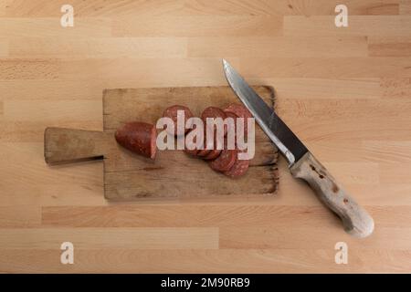 Draufsicht auf Wurstscheiben und Messer auf Holzhackbrett. Stockfoto