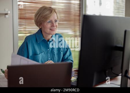 Eine lächelnde, reife Ingenieurin arbeitet vom Heimbüro aus mit einem Computer an einem Projekt Stockfoto