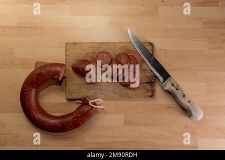 Messer und Wurstscheiben auf Holzbrett in der Draufsicht. Stockfoto