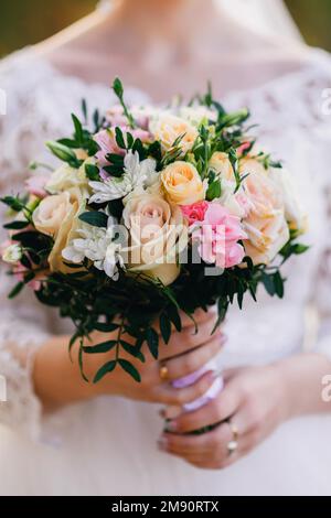 Wunderschöner Hochzeitsstrauß mit gelben Rosen, weißen Chrysanthemen und rosa Alstroemeria in den Händen der Braut in einem weißen Kleid Stockfoto