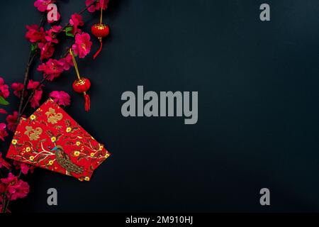 Dekoration im chinesischen Neujahrsmond auf schwarzem Hintergrund. Flach liegendes Konzept mit rotem Umschlag und Pflaumenblütendekoration. Stockfoto