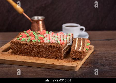 Selektiver Fokus auf Kekskuchen mit bunten Buttercreme-Blumen. Eine Tasse Kaffee ist im Hintergrund verschwommen. Stockfoto