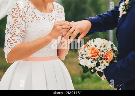 Die Braut trägt bei der Hochzeit einen Ring am Finger des Bräutigams Stockfoto