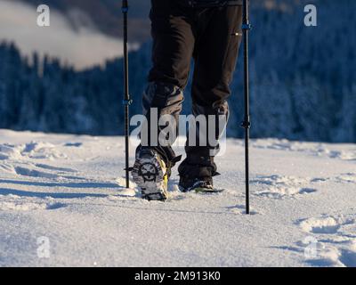 Nahaufnahme eines Mannes, der auf einem schneebedeckten Berg wandert, in Stiefeln mit Schuhpikes. Wanderung im Winter im Freien Stockfoto