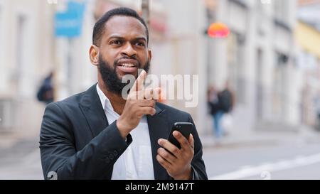 Afroamerikanischer bärtiger Mann mit Smartphone, der auf den Bildschirm des Mobiltelefons schaut. Suchen Sie mit der elektronischen Online-Karten-App in der Stadt nach der Adresse. Ethnisch männlich Stockfoto