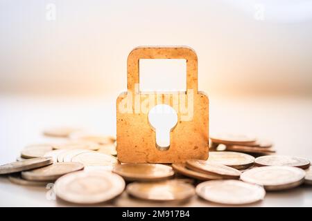 Geld- und Sicherheitskonzept. Ein Schlüsselsymbol aus Holz auf einem Haufen Münzen. Stockfoto