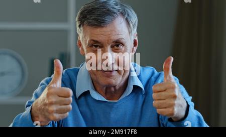 Nahaufnahme Erfolg glücklicher, reifer, alter, weißer Mann, der zwei Daumen hoch zeigt lächelnder Rentner, der in die Kamera schaut, demonstriert wie eine gute Idee Stockfoto