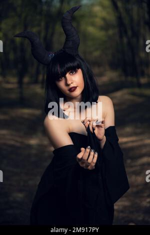 Ein vertikales Bild eines gotischen Mädchens mit Maleficent-Hörnern, das in einem mystischen Wald posiert Stockfoto