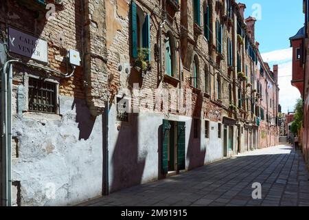 Malerische alte Fassade in Venedig, Italien. Details der veralteten Ziegelwand mit Pflanzen getönten Fenstern. Auf dem Schild links steht "Venier's Stockfoto