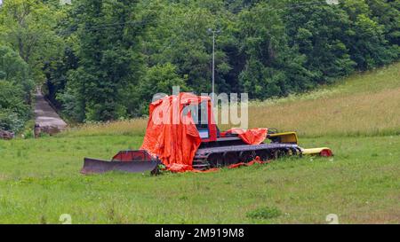 Schneeräumer unter Plane parkt im Sommer auf dem Grasfeld Stockfoto