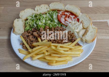 Bistro Dishe kulinarisches Stillleben. Kalbsnuss mit Salat, Tomaten-Beilagen-Zwiebel, pommes frites und eine Scheibe Brot Stockfoto