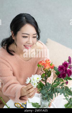 Die junge Frau zu Hause, die Blumen arrangiert Stockfoto