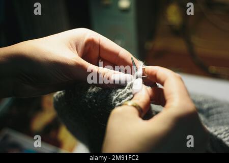 Nahaufnahmen von Händen, die das Kleid aus leichter Wolle auf verschwommenem Hintergrund stricken. Mit kreisförmigen Nadeln Stockfoto