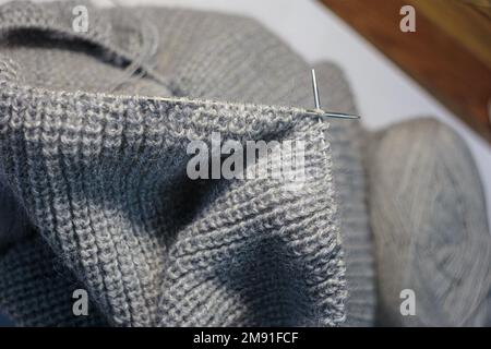 Stricken der Kleidung mit kreisförmigen Nadeln. Auf grauem, verschwommenem Hintergrund. Draufsicht Stockfoto