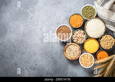 Glutenfreies Müsli. Verschiedene Schüsseln mit Reis, Buchweizen, Mais, Linsen, Sojabohnen und Quinoa am Steintisch. Draufsicht mit Kopierbereich. Stockfoto