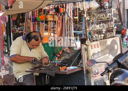 Georgetown, Penang, Malaysia - November 2012: Ein Mann bei der Arbeit in einer Straßenwerkstatt in einer Marktstraße. Stockfoto