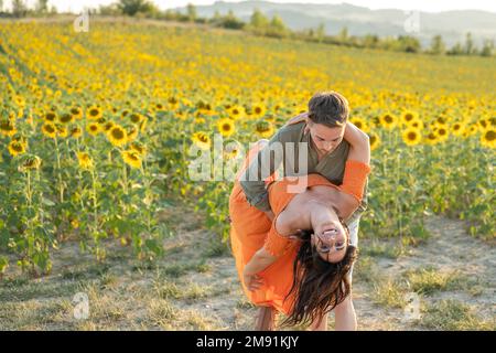 Junge Liebespaare, die draußen auf einem Feld voller Sonnenblumen tanzen, sei mein valentinstag-Konzept Stockfoto