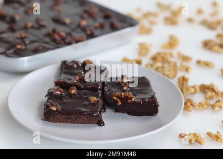 Ein Stück Texas Sheet Cake, serviert auf einem Teller. Es ist ein großer, dünner Schokoladenkuchen, gekrönt mit einem reichen Schokoladen-Walnussschaum. Es ist feucht und flauschig, w Stockfoto