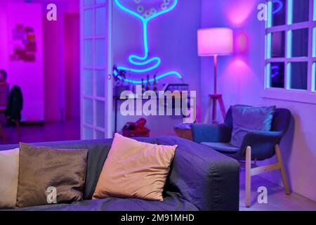 Geräumiges Wohnzimmer mit Neonlicht und weicher, komfortabler Couch in der Mitte, umgeben von Sessel und kleinem Tisch mit alkoholischen Getränken Stockfoto