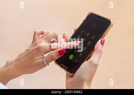 Goiania, Goiás, Brasilien – 10. Januar 2023: Details weiblicher Hände, mit rot lackierten Nägeln, mit einem Handy in der Hand, Wählen einer Nummer. Stockfoto