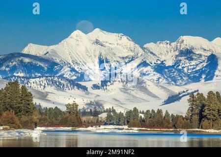 Der Vollmond erhebt sich im Winter über den Flathead River und die Mission Mountains in der Nähe von dixon, montana Stockfoto