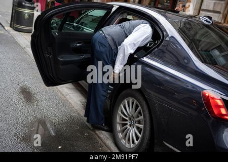 Am 16. Januar 2023 in London, England, lehnt sich ein Autofahrer in das Heck eines dunklen Autos in der Jermyn Street. Stockfoto