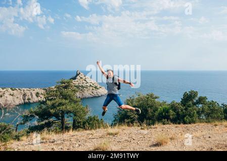 Männlicher Reisender springt freudig und glücklich in die Natur im Sommerurlaub in den Bergen am Meer und symbolisiert die Freiheit Stockfoto