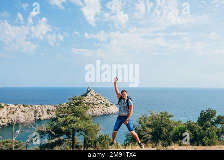 Männlicher Reisender springt freudig und glücklich in die Natur im Sommerurlaub in den Bergen am Meer Stockfoto