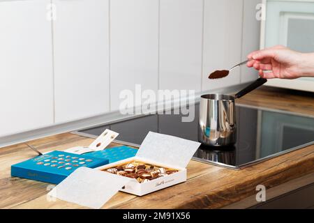 Zürich, Schweiz - Januar 7 2023: Lindt Mini Pralines Box. Offene kleine Geschenkbox mit Schweizer Schokoladensorten und eine Hand junger Frau, die türkischen Kaffee auf der Küchenplatte macht. Stockfoto