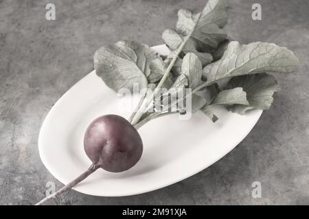 Frischer Rettich mit grünen Blättern auf dem Tisch in einer weißen Keramikplatte Stockfoto