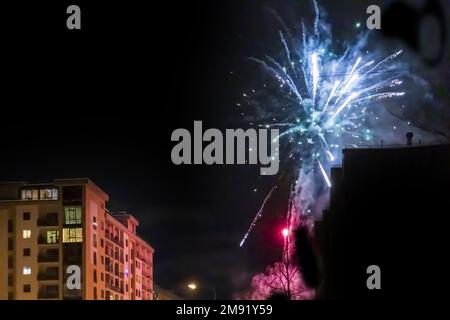 Ein farbenfrohes Raketenfeuerwerk vor einem Stadthaus vor einem dunklen Himmel Stockfoto