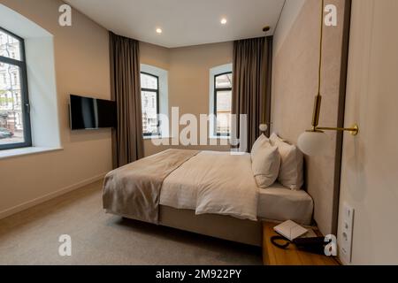 Telefon in der Nähe eines komfortablen Bettes mit weißer Bettwäsche im Hotelzimmer, Stockbild Stockfoto