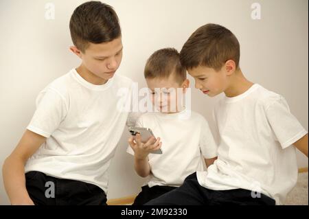 Kinder unterschiedlichen Alters sehen sich Telefone mit Interesse an. Soziale Netzwerke sehen sich Videos und Fotos auf dem weißen Großbildschirm von Telefonbrüdern an Stockfoto