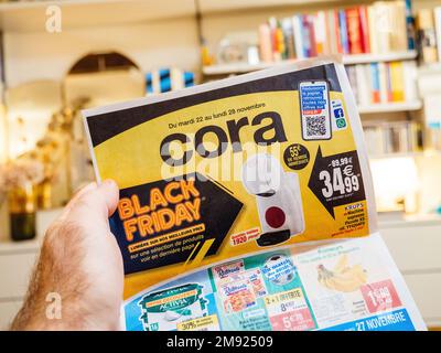 Paris, Frankreich - 2. Dez. 2022: Mann liest Werbebroschüren der Cora Supermarktkette, die Möbel, Elektronik-Gegenstände verkauft Stockfoto