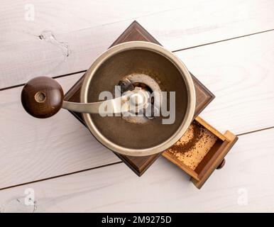 Manuelle Kaffeemühle auf einem weiß lackierten Holztisch, Draufsicht. Stockfoto