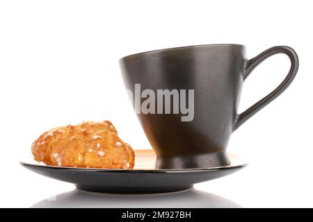 Eine süße Chouquette mit einer Tasse auf einer Untertasse, Nahaufnahme, isoliert auf Weiß. Stockfoto