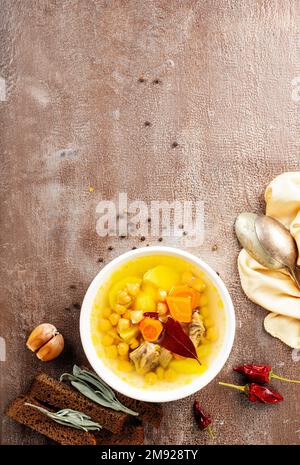 Heiße würzige Suppe mit Kichererbsen, Zwiebeln in Keramikschüssel auf dunklem Hintergrund. Stockfoto
