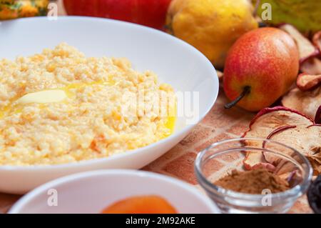 Kürbisbrei mit Hirse, Milch und Zimt. Nahaufnahme von Kürbisbrei mit Hirse, serviert in einer weißen Schüssel, selektiver Fokus, horizontaler Schuss. Stockfoto