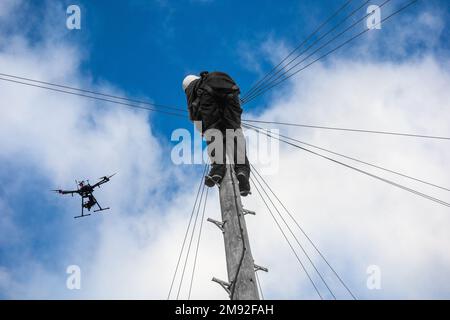 Telekommunikations- und Telekommunikationsingenieur arbeiten am Telegrafenmast mit der Drohne, die über uns fliegt. Drohnen-Technologie, Breitband, 5G, Internet... Konzept. UK Stockfoto