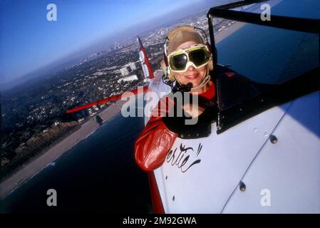 Pilot Bertie Duffy fliegt in ihrem offenen Cockpit 1941 Stearman über den Strand von Santa Monica mit Downtown L.A. und Smoggy Sky im Hintergrund, Los Angeles, Kalifornien, USA Stockfoto