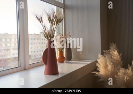 Getrocknete Blumen in einer alten Keramikvase am Fenster. Sonnenlicht und Sonnenlicht fallen vom Fenster. Minimalismus im Innenraum. Platz zum Kopieren. Hochwertiges Foto Stockfoto