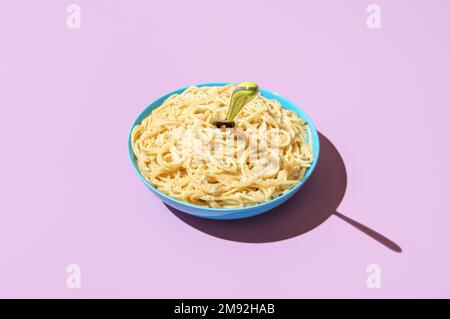 Schüssel mit Spaghetti cacio e pepe Minimalist auf einem Tisch in leuchtenden Farben. Spaghetti mit Parmesan und schwarzem Pfeffer auf violettem Hintergrund Stockfoto