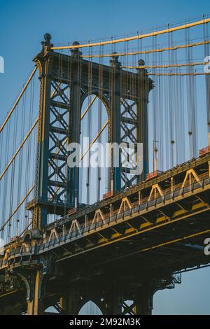 Unter der berühmten Manhattan Bridge mit Metallkonstruktionen unter blauem wolkenlosem Himmel in New York City bei Sonnenuntergang Stockfoto
