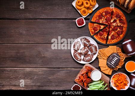 Super Bowl- oder Football-Themen, Food Side Border. Pizza, Hamburger, Flügel, Snacks und Beilagen. Ansicht von oben auf dunklem Holzhintergrund. Stockfoto