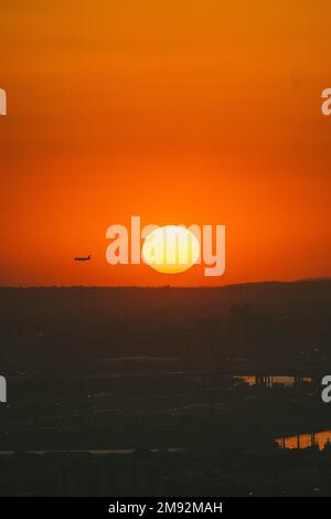 Malerischer Blick auf den farbenfrohen, orangefarbenen Sonnenuntergang mit der runden, großen gelben Sonne und dem fliegenden Flugzeug Stockfoto