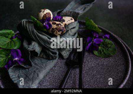 Frühlingstisch mit wilder blauer Veilchenblume auf schwarzem Teller Stockfoto